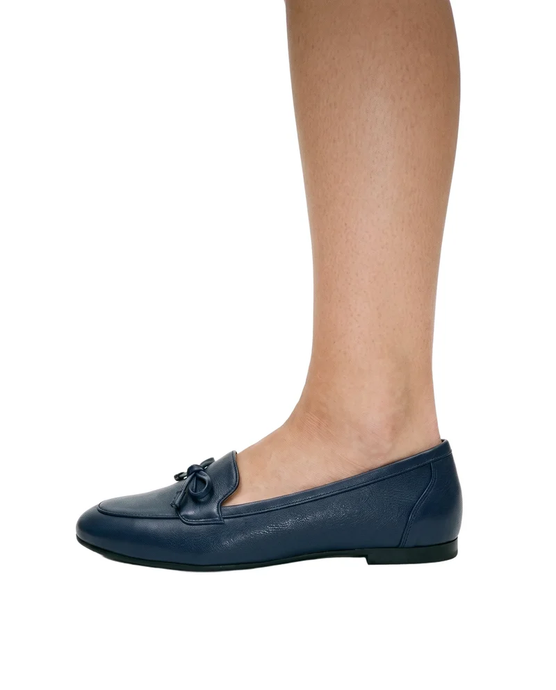 Women's navy loafers shown from the side with the foot flat, cropped at the ankle against a pure white backdrop.