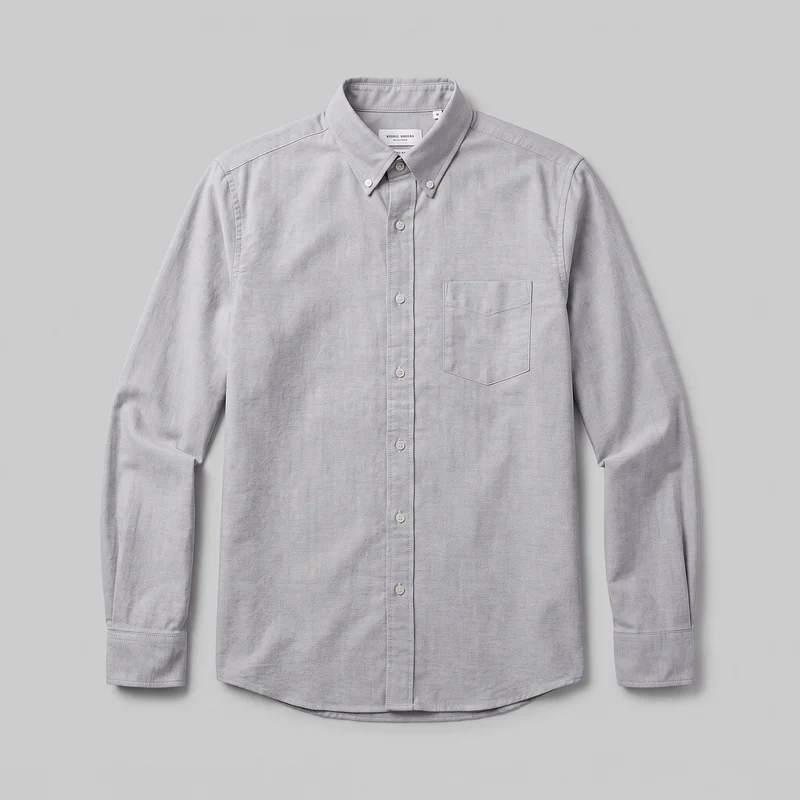Grey cotton Oxford shirt shown laid flat in a complete front view. It has a structured button-down point collar, a full central button placket, long sleeves with button cuffs, a single patch chest pocket, and a curved shirttail hem.