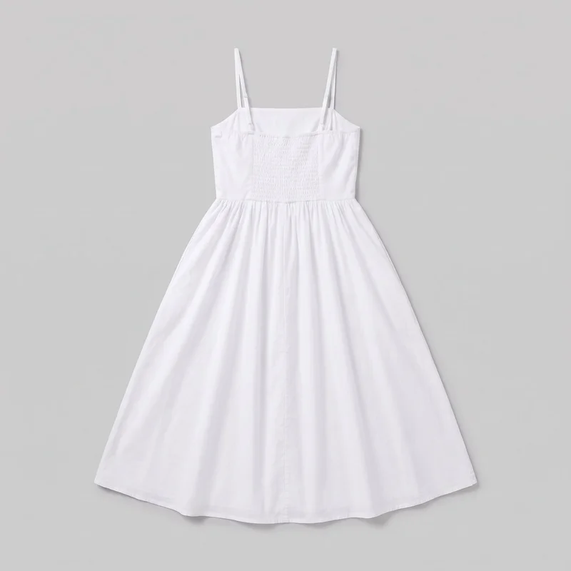 A mostly complete front view of a white cotton women's sundress laid flat. The sleeveless dress has narrow adjustable shoulder straps, a straight square neckline, a rectangular smocked center bodice panel, smooth side panels, a defined waist with gathering, and a full flared A-line skirt with a center-front button placket extending toward the below-knee or midi-length hem.