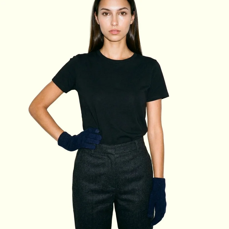 A 21-year-old Slavic woman is shown from the upper body in a front-facing pose with one hand on her hip, wearing women's navy touchscreen gloves. Her expression is neutral, and an ivory lace backdrop frames the studio-cutout composition.