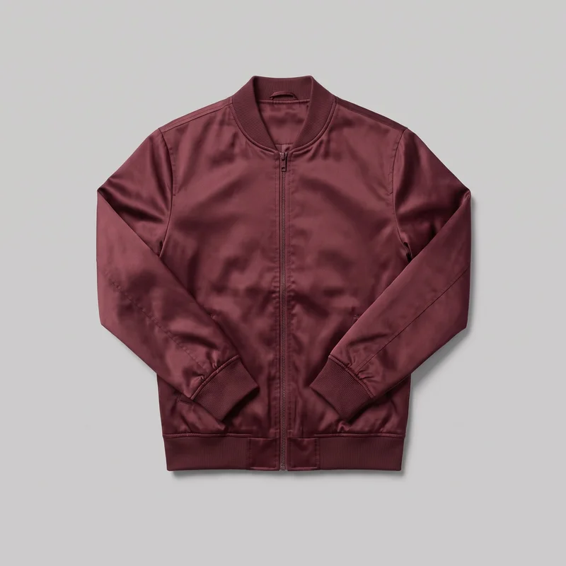 A mostly complete front view of a men's burgundy satin bomber jacket laid flat against a backdrop. The jacket has a ribbed bomber collar, full-length sleeves with ribbed cuffs, shoulder and sleeve seam panels, a centered full-length zipper with a visible pull, lower front welt pockets, and a straight ribbed hem band. No logos, prints, patches, embroidery, or embellishments are visible.