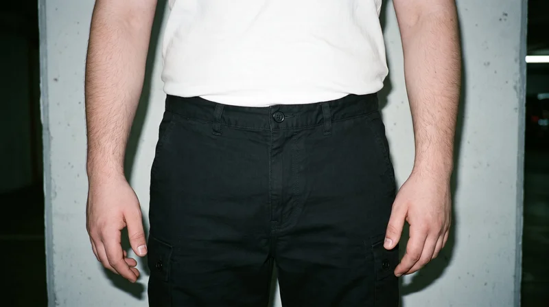 Men's black cargo shorts shown from the front in a level-hip crop, with a concrete parking garage backdrop.