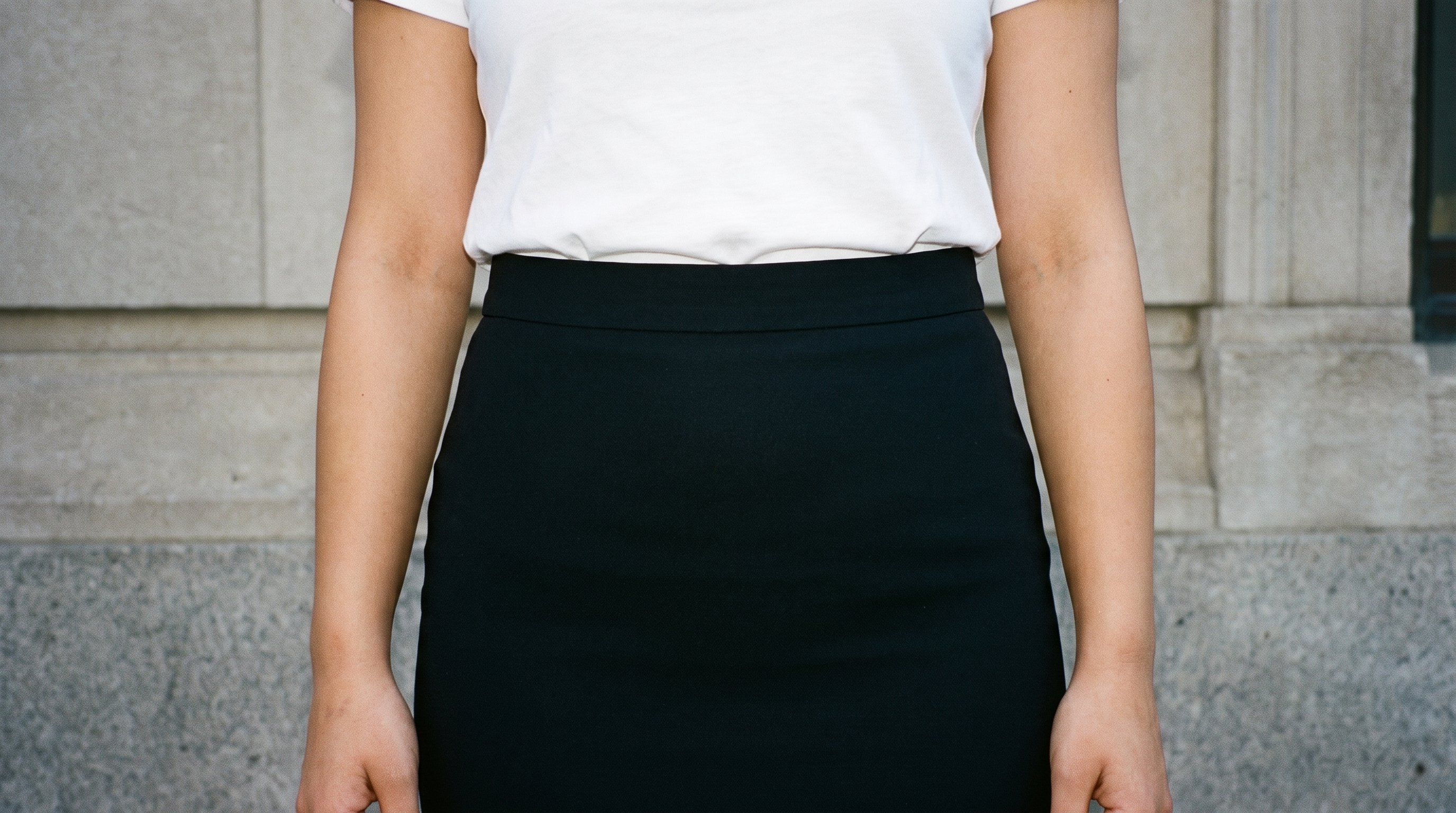 A model's hips are shown from the front at a level pose, wearing a black midi skirt. The background is Fountain Plaza.