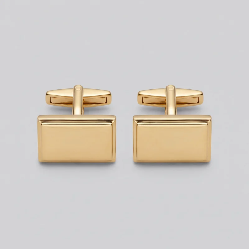 A matching pair of gold cufflinks is shown as a standalone product. Each cufflink has a smooth rectangular face plate with softly rounded corners, raised beveled edges, and a plain flat center, along with a vertical connector stem and a horizontal T-bar toggle with rounded ends and an inset rectangular recess. The front face plates and T-bar backs are both visible.