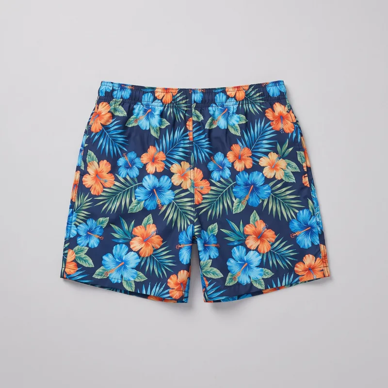 Standalone swim shorts shown in a mostly complete flat front view. The shorts have a relaxed straight-leg silhouette, a gathered multi-channel elastic waistband with horizontal stitching, above-knee straight hems, a vertical center front seam, visible side pocket openings, and an all-over tropical hibiscus flower and palm-leaf print.