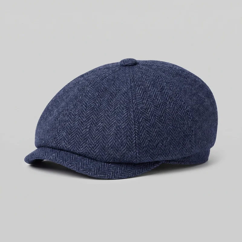 A women's navy newsboy cap is shown alone from an angled view. It has a rounded, full paneled crown with vertical seams converging at a covered top button, a narrow lower band, and a short curved front brim partially tucked beneath the front edge. The fine herringbone pattern is visible across the surface, with no logos, patches, embroidery, or embellishments.