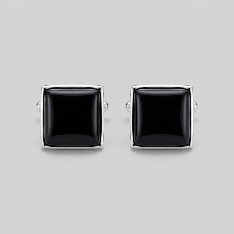 A matching pair of cufflinks is shown from the front against a plain backdrop. Each cufflink has an upright rectangular face with rounded corners, beveled edges, a raised softly domed rectangular center, a narrow recessed border, and a rounded rectangular outer rim. Partial post-and-toggle hardware is visible behind the faces.