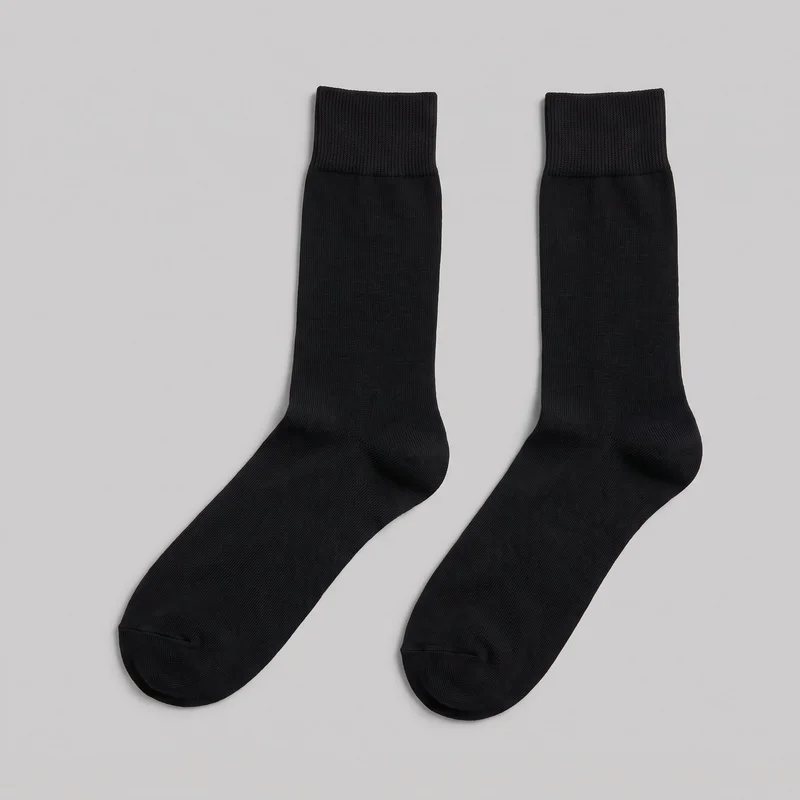 A pair of black calf-height crew socks is laid flat, with both complete sock shapes visible from the wide ribbed top cuffs through the smooth fine-knit legs and feet. The socks have tubular legs, shaped heels, rounded closed toes, and visible toe seams or reinforced toe areas.