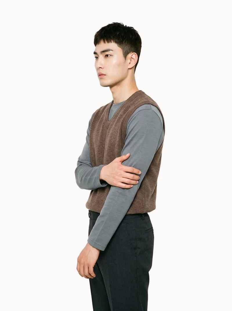 A 26-year-old Korean man is shown in a three-quarter-length side view wearing a brown wool sweater vest. He holds one arm in a natural pose, with a Chantilly Lace flat-color backdrop.
