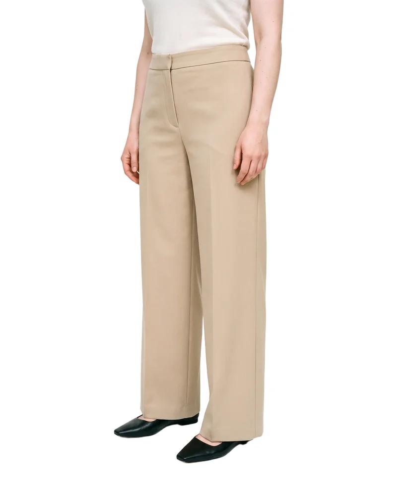 Beige wide-leg trousers on a female model, framed from the lower body at a front three-quarter angle with her feet together. The trousers are shown against a pure white backdrop.