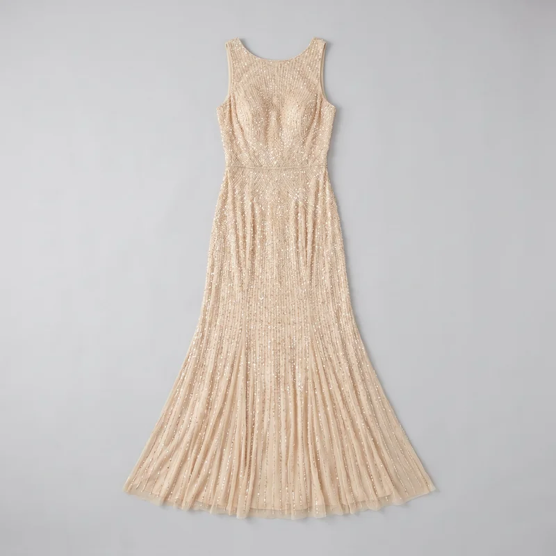 A champagne-colored sleeveless evening gown is shown laid flat in a complete front view. It has wide shoulder straps, a rounded scoop neckline, a fitted body-skimming bodice with a defined waist, and a floor-length mermaid skirt that flares toward the hem. Dense vertical beaded or sequined striping and scattered reflective embellishments cover the gown.