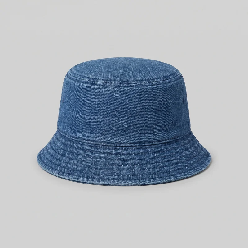 A standalone men's denim bucket hat is shown from a front-facing, slightly elevated angle against an unspecified backdrop. It has a rounded cylindrical crown, a flat circular top, a horizontal seam band below the top, and another seam where the crown meets the brim. Small ventilation eyelets appear on the side panels, while the structured downward-sloping brim features multiple concentric rows of topstitching and a narrow finished outer edge. No logos, prints, patches, embroidery, or embellishments are visible.