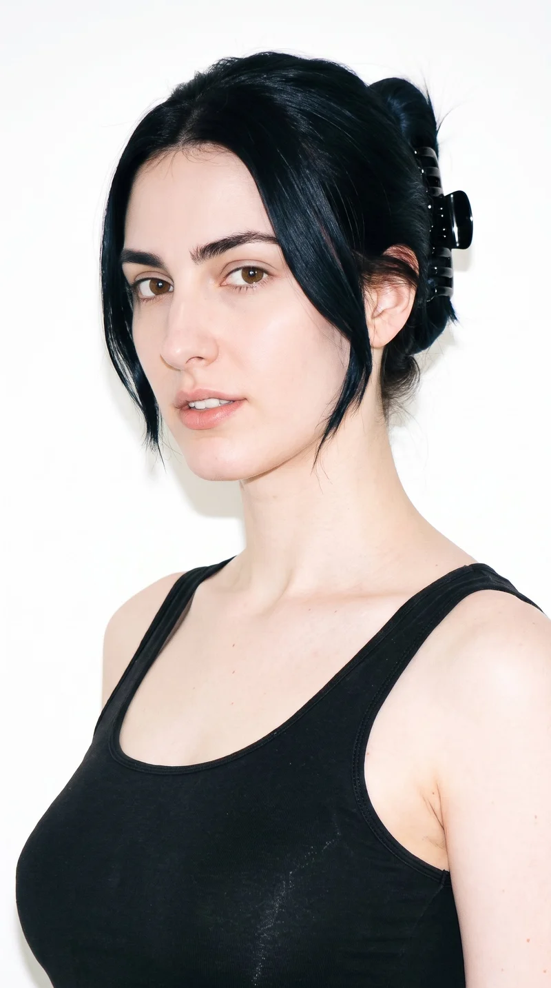 This 23-year-old Caucasian woman has porcelain skin with a neutral undertone. Her triangle-shaped face has a wide jaw that narrows toward the forehead, emphasizing the lower face. She has thick eyebrows, brown eyes, and thin lips. Her deep black hair is twisted up and secured with a claw clip, with relaxed ends.
