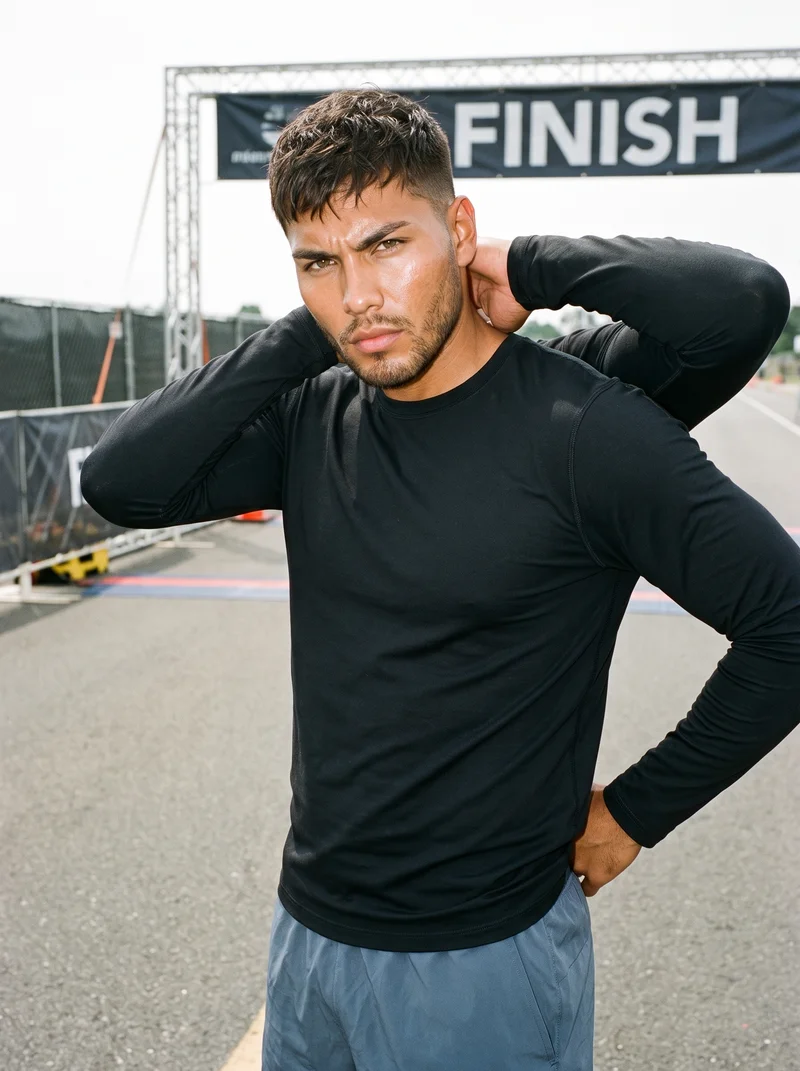 A 24-year-old Indigenous American man wears a men's black compression base layer in an upper-body composition. He is shown from a front three-quarter angle with one hand behind his neck and an intense facial expression. A marathon finish line forms the backdrop.
