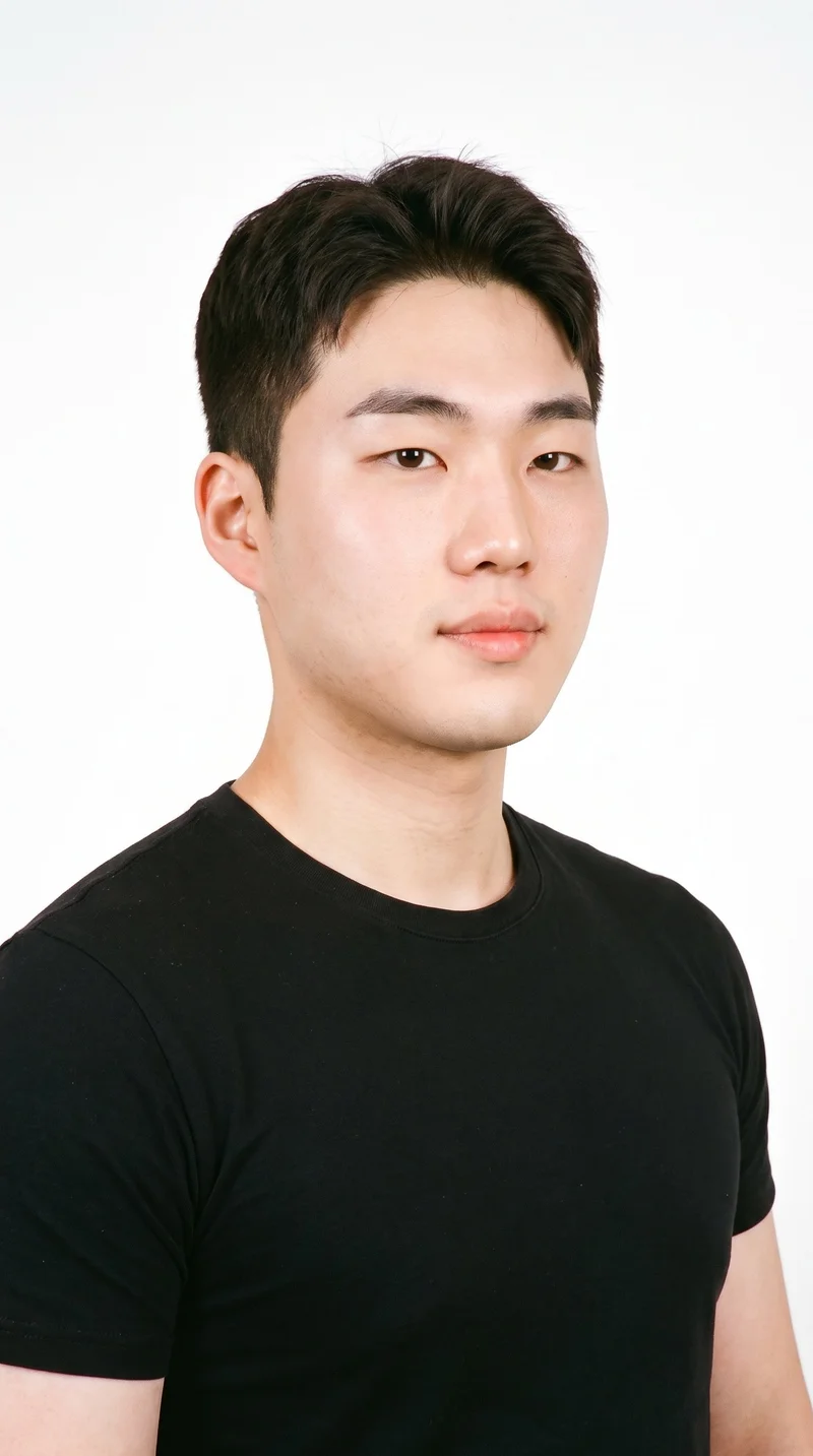 A 21-year-old Korean man with fair skin and a warm yellow undertone has a round face with soft, full contours and few angles. His thick eyebrows frame very dark, near-black eyes, and he has full lips. His dark-brown hair is styled in a short, tapered crew cut, slightly longer on top than at the sides. Fine, closely trimmed stubble lightly covers the beard area.