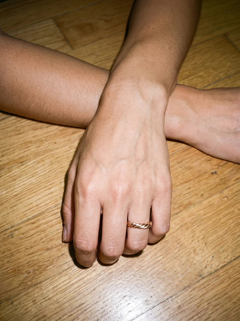 A hand and wrist wearing a women's rose gold stacking ring, shown from above with the knuckles facing forward. The dance studio serves as the backdrop.