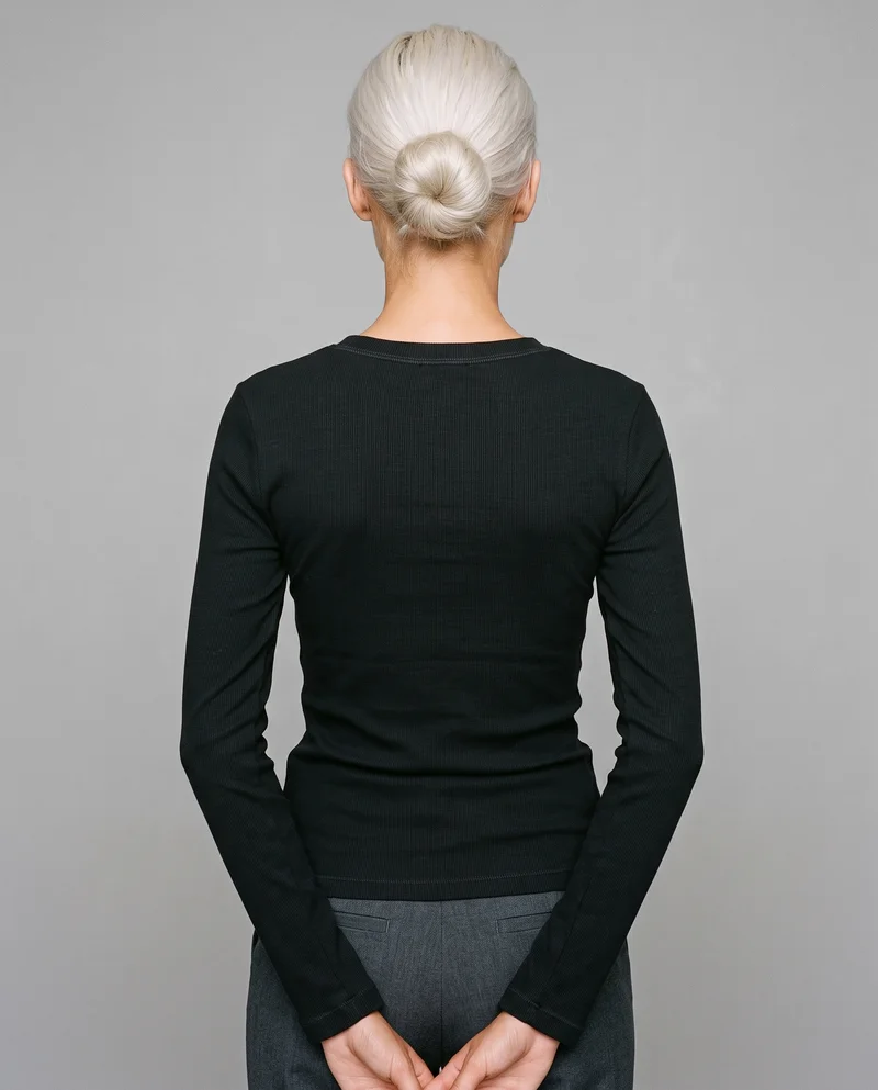 A 22-year-old Caucasian woman is shown from the upper body in a back view, wearing a women's black thermal top with her hands behind her back. The image uses a Pebble Grey studio-wall backdrop.