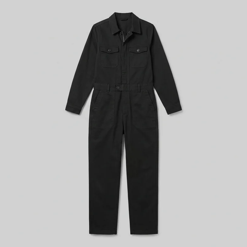 A black women's utility boilersuit is shown laid flat in a full front view. The long-sleeve coverall has a pointed fold-down collar, a front zipper and buttons, a defined waist with belt loops, two buttoned chest pockets, and two large lower patch pockets beneath angled side openings. Straight full-length legs and visible seam stitching complete the design.