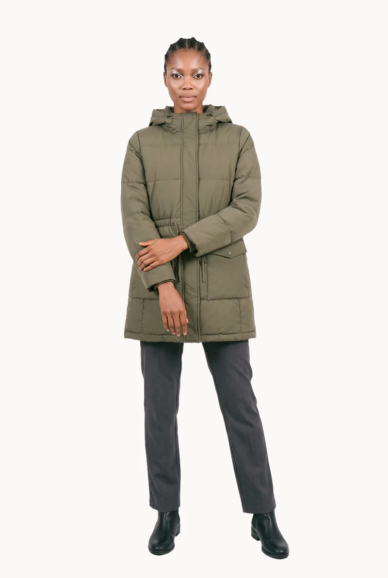 A 26-year-old African woman is shown full body from the front wearing a women's olive padded parka. Her arms are held low and her expression is natural, with a Chantilly Lace flat-color backdrop.
