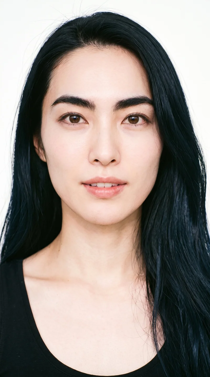 A 36-year-old Japanese woman with a light porcelain skin tone and cool undertone has a heart-shaped face, with a wider forehead narrowing to a more pointed chin. Her eyebrows are thick, and her eyes are very dark, near-black. She has medium lips and long black hair worn loose past the shoulders with natural volume.