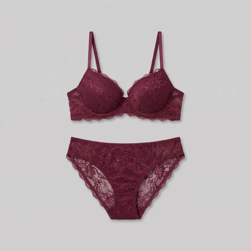 A burgundy lingerie set is arranged as a flat lay, with the matching bra and brief shown separately and mostly complete. The bra has structured underwire cups, a low center gore, narrow shoulder straps, scalloped trim, and an all-over floral lace pattern with denser motifs over sheer areas. The mid-rise brief has a full front panel, curved leg openings with scalloped lace edging, a narrow finished waistband, sheer side panels, and matching floral lace.