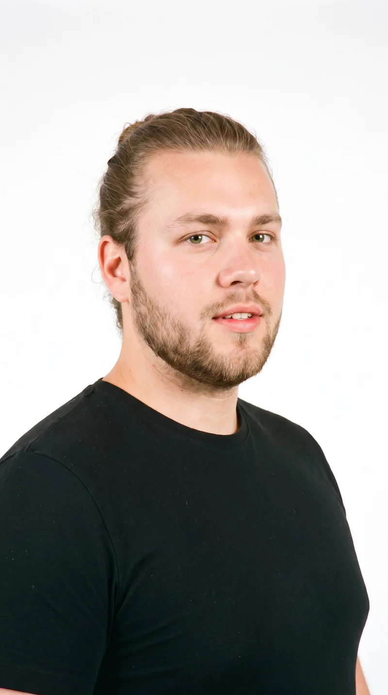 This 22-year-old Caucasian man has a medium skin tone with a neutral undertone and an oval face with balanced proportions and a softly rounded jaw. His medium-thickness eyebrows frame green eyes, and he has medium-sized lips. His light-brown hair is gathered into a knot at the back with the sides drawn up. A short, structured beard with defined edges follows his cheeks and jaw.