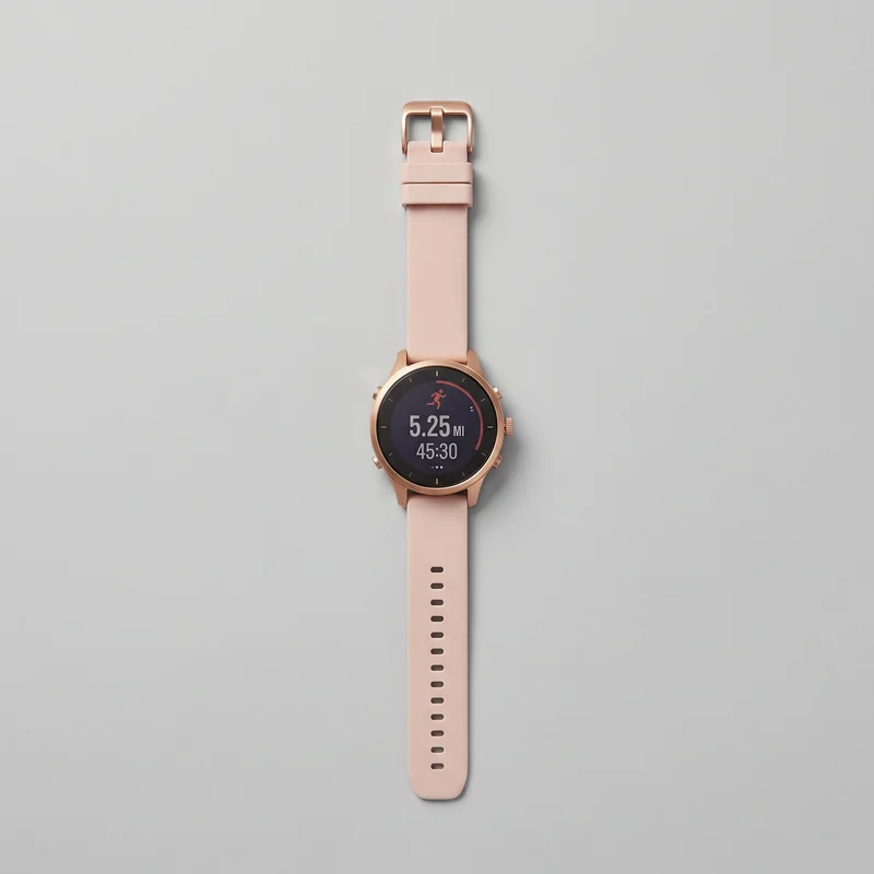 A complete unisex GPS sports smartwatch lies flat in a top-down view, with a round digital watch face, slim circular bezel, short lugs, and a straight two-piece strap. The display shows tick markers, a running icon, distance, and time readout. A ridged crown and additional pushers are visible on the case side, while the strap shows a rectangular tang buckle, keeper loop, and oval adjustment holes.