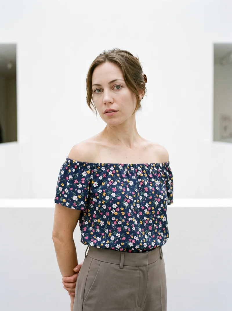 A 31-year-old Caucasian woman wears a Floral Print Bardot Top in an upper-body view from a front three-quarter angle. Her hands are behind her back and her expression is neutral, with a Contemporary Art White Atrium backdrop.