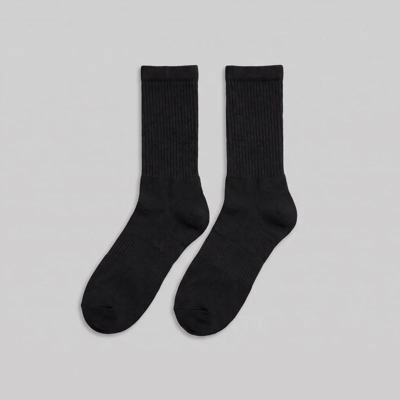 A pair of black crew-length socks is laid flat with both full shafts, heels, and rounded toes visible. The socks have straight ribbed leg sections, thicker ribbed opening bands, smooth foot areas, shaped heels, and visible toe seams. No logos, prints, patches, embroidery, or embellishments are visible.