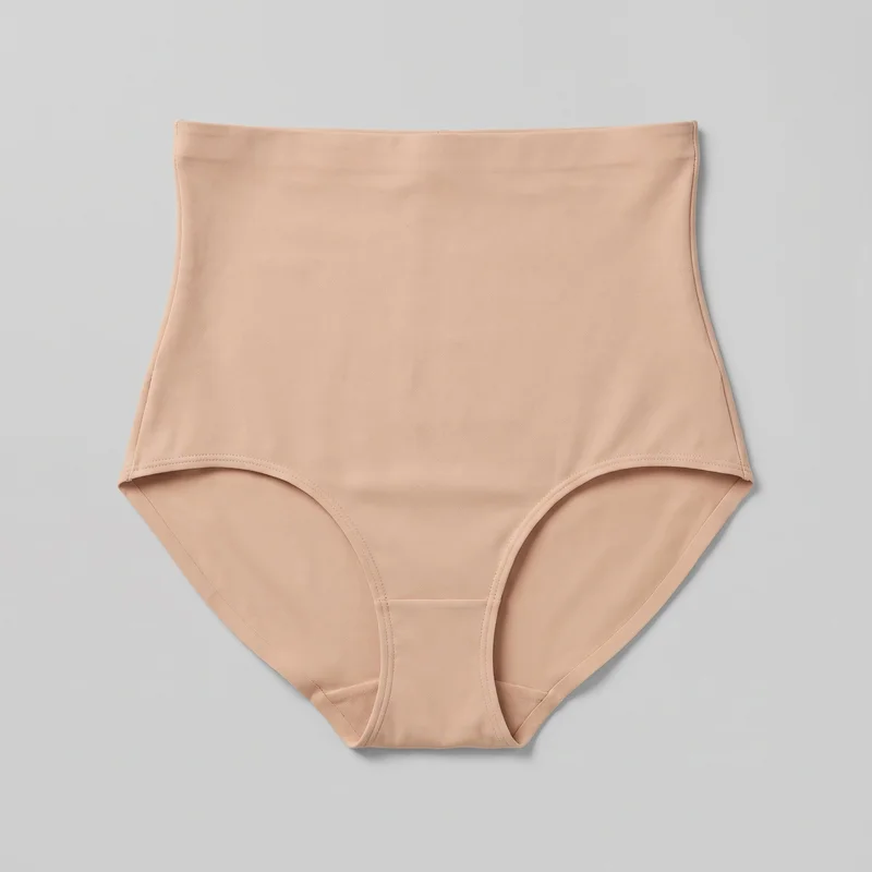 A complete flat-lay view of nude high-waisted brief underwear is shown, with the full outline from the straight waistband through the curved leg openings visible. The brief has smooth paneling, vertical side seams, a narrow center gusset panel, and stitched binding around the waistband and leg openings.