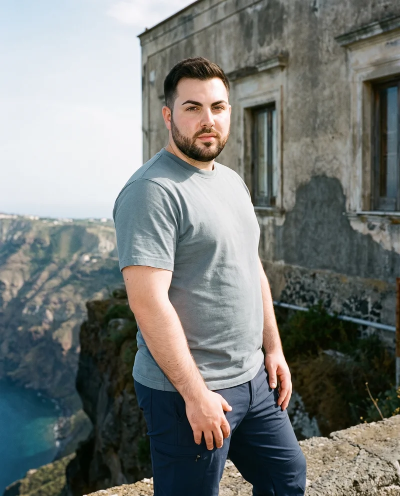 A 28-year-old Caucasian man wears navy hiking trousers in a three-quarter-length frame, viewed from a front three-quarter angle with his waist twisted. A Santorini caldera view forms the backdrop.