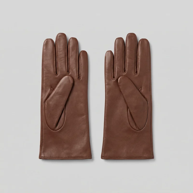 A complete pair of brown leather five-finger dress gloves is laid flat with the fingers upright and the separate thumbs angled inward over the palm areas. The gloves have close-fitting silhouettes, tapered rounded fingers, extended straight cuffs with flat bottom hems, raised edge piping, stitched channels between the fingers, oval thumb-seam panels, narrow side seams, and stitched cuff hems. No closures, logos, prints, patches, embroidery, or embellishments are visible.
