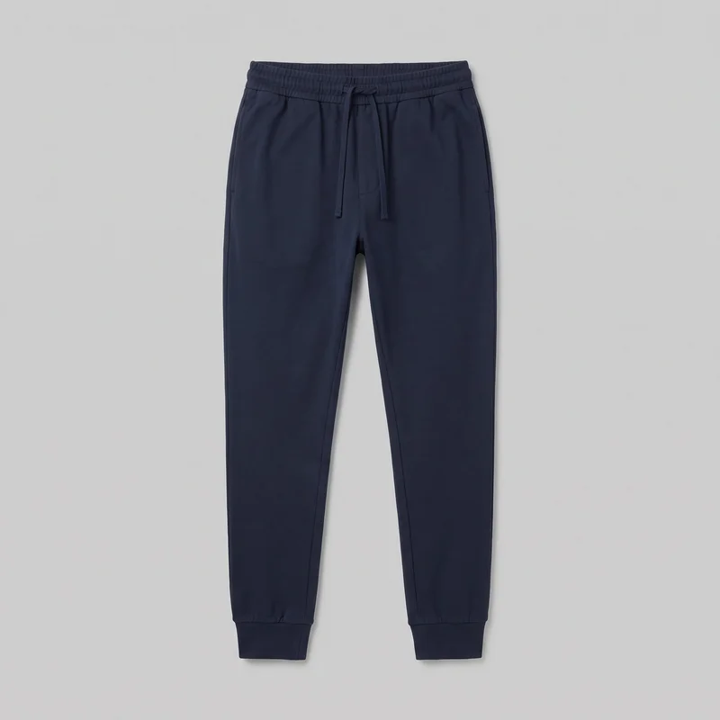 Men's navy cotton jogger sweatpants shown in a full front standalone view. The pull-on trousers have a gathered elastic waistband with a center front drawstring, a faux fly seam, angled upper side-entry pockets, tapered full-length legs, vertical side seams, and ribbed ankle cuffs.