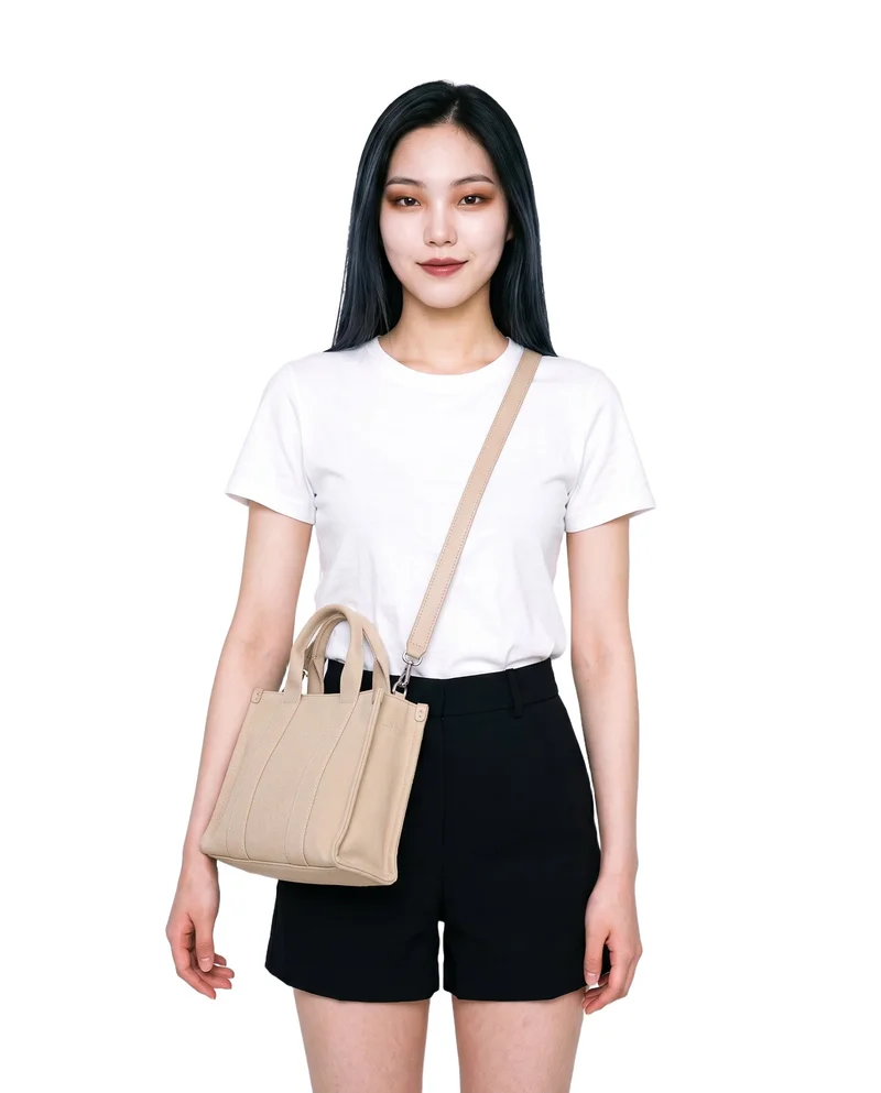 A 19-year-old Korean woman stands straight in a front-facing three-quarter-length view, wearing a beige canvas crossbody bag. The bag is shown against a pure white backdrop.