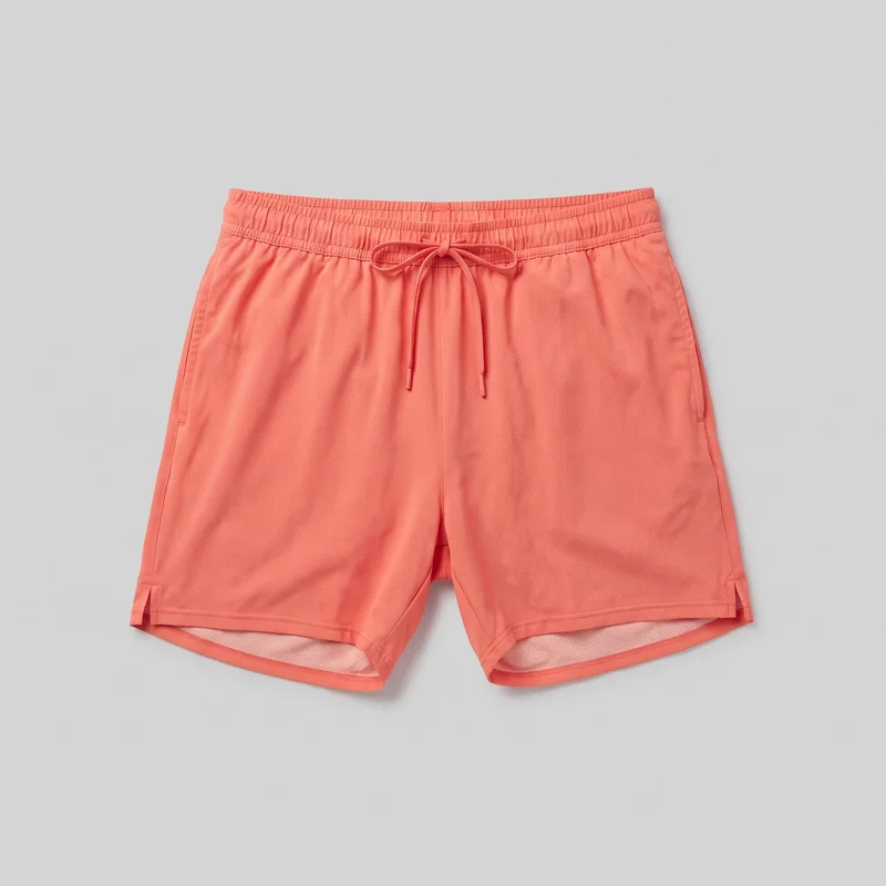 Coral pull-on running shorts shown alone in a complete front-facing view. The shorts have a relaxed straight-leg silhouette, an above-knee cut, an elastic gathered waistband, and an exterior round drawstring tied in a bow at the center front. Vertical side seams, front slash pockets, a visible center-front rise seam, straight double-stitched hems, short reinforced side hem vents, and the built-in inner liner visible at the leg openings are shown. The exterior has a fine allover perforated texture with no visible logos, prints, patches, embroidery, or embellishments.