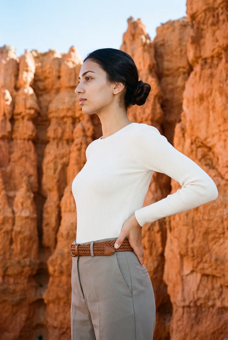 An 18-year-old Turkish woman is shown in a three-quarter-length side view with her hands on her waist and a neutral expression, wearing a tan woven leather belt. Bryce Canyon hoodoos form the backdrop.