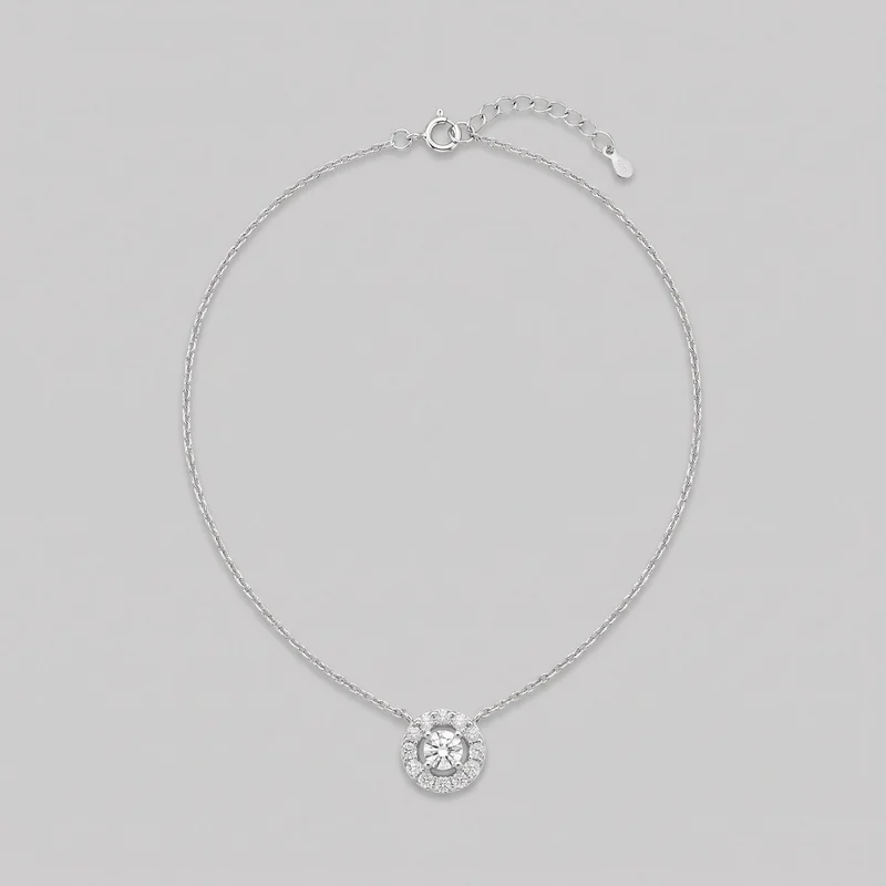 A fine women's chain necklace is laid in an oval shape, with a round pendant centered at the bottom. The pendant features a raised faceted central stone held by prongs, surrounded by an open ring and an outer halo of smaller stones. The spring-ring clasp, extender chain, jump rings, and small end tag are visible at the top.
