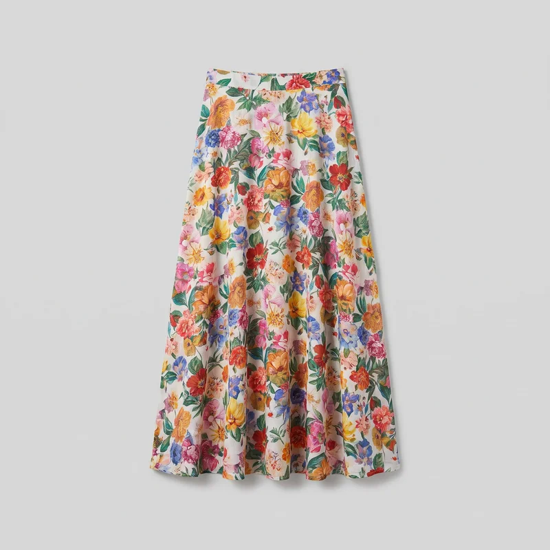 A standalone front view of a long A-line maxi skirt with a flat fitted waistband, a full flared silhouette, vertical folds, and panel or seam shaping below the waist. The skirt features an all-over floral and leaf print and ends in a wide straight hem.
