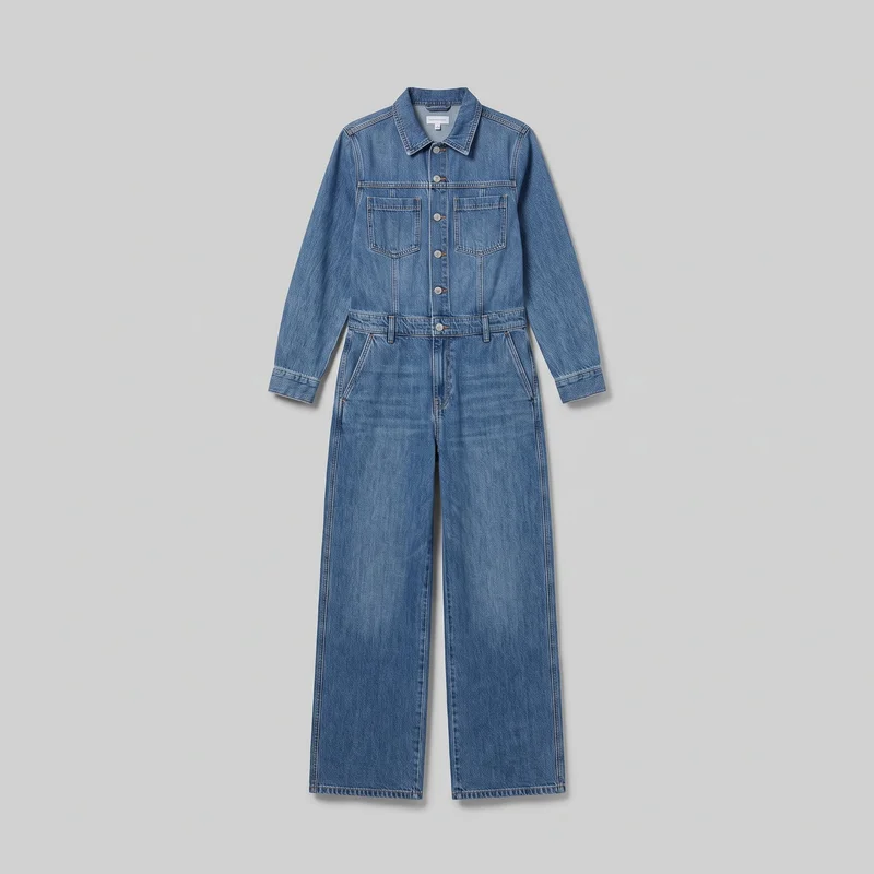A one-piece denim utility jumpsuit is shown laid flat in a full front view. It has a pointed shirt-style collar, long sleeves with button cuffs, a central button placket with round metal buttons, two square chest patch pockets, a high waist seam with belt loops, slanted hip pockets, visible panel seams, contrast topstitching, and full-length straight wide legs with straight hems.