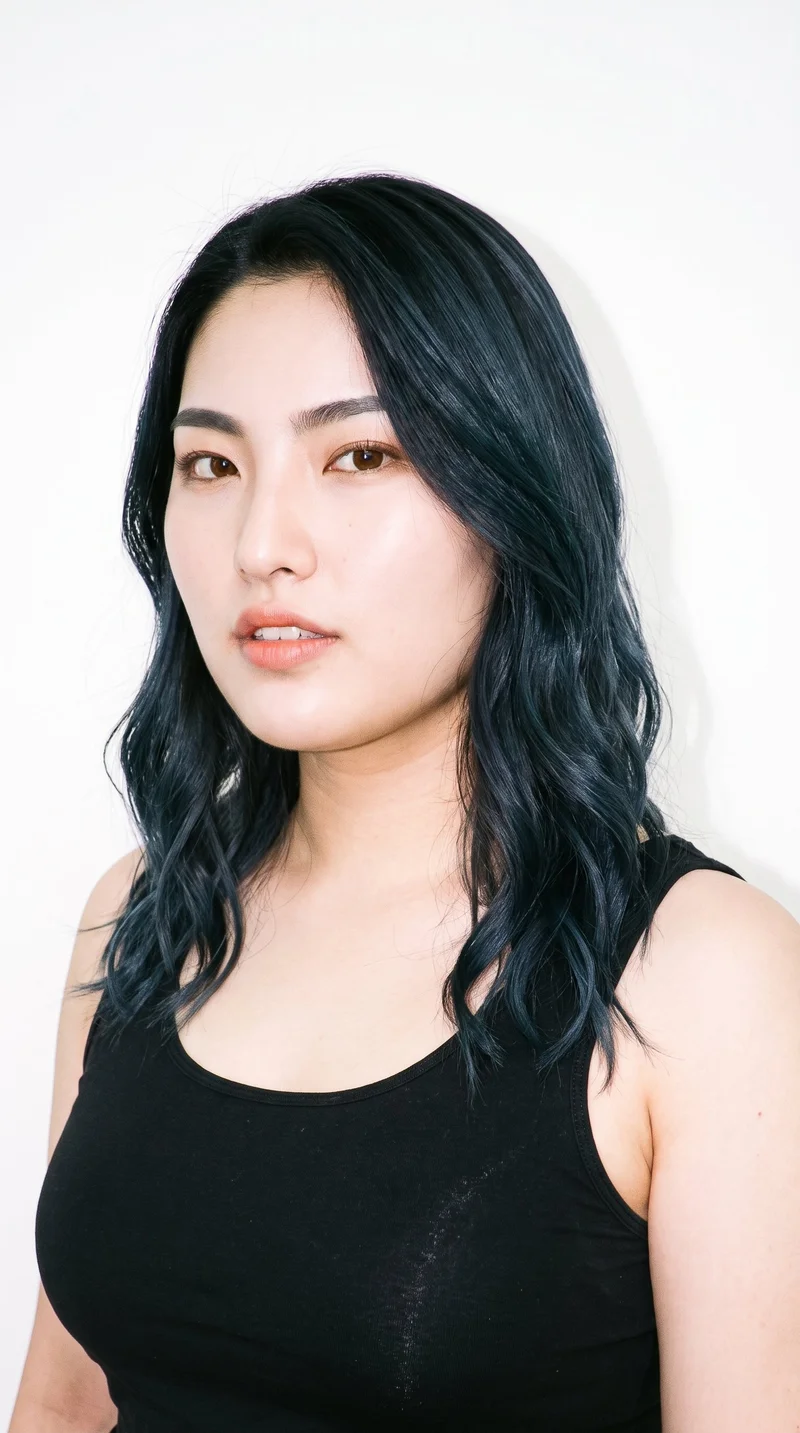 This 22-year-old Japanese woman has a light porcelain skin tone with a cool undertone. Her diamond-shaped face has a narrow forehead and jaw and is widest at the cheekbones. She has thick eyebrows, brown eyes, and full lips. Her deep black hair falls in loose, slightly tousled waves with natural volume.