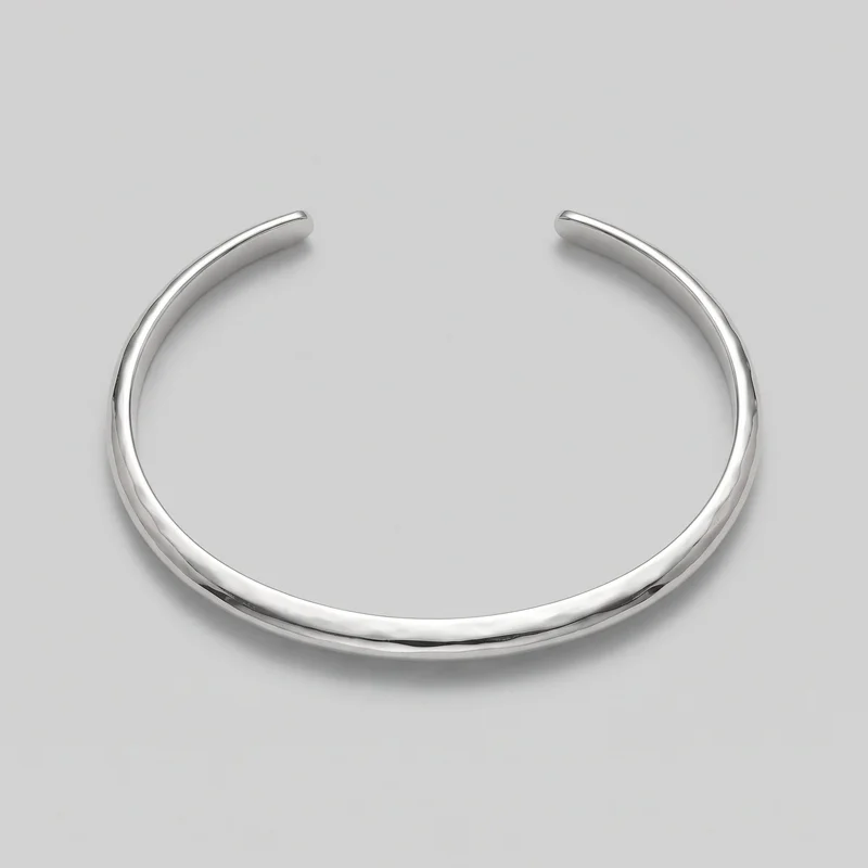 A complete silver open cuff bracelet is shown alone from an overhead angled view. The rigid C-shaped band has two blunt rounded terminals, a rounded tubular profile, softly beveled edges, and a smooth polished surface with subtle organic undulation along the sides. No clasp, hinge, stones, logo, print, or other embellishment is visible.
