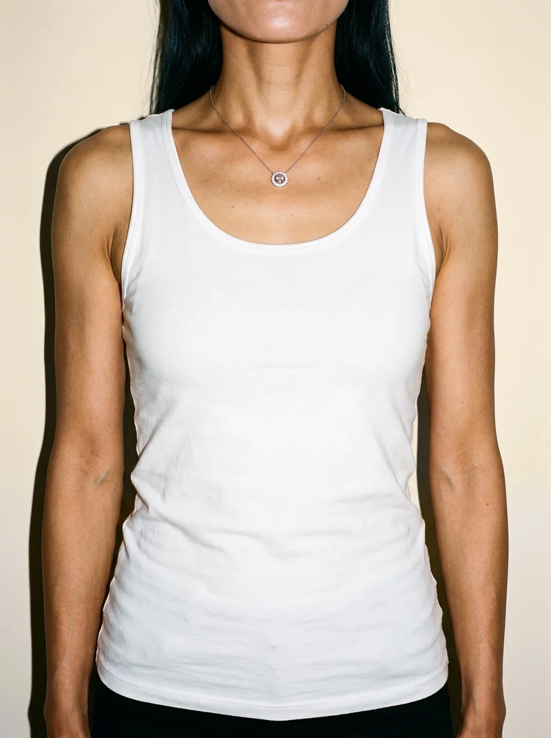 A woman is shown from the front in a torso-length view wearing a women's diamond pendant. Her arms are relaxed, and a cream silk backdrop fills the studio setting.