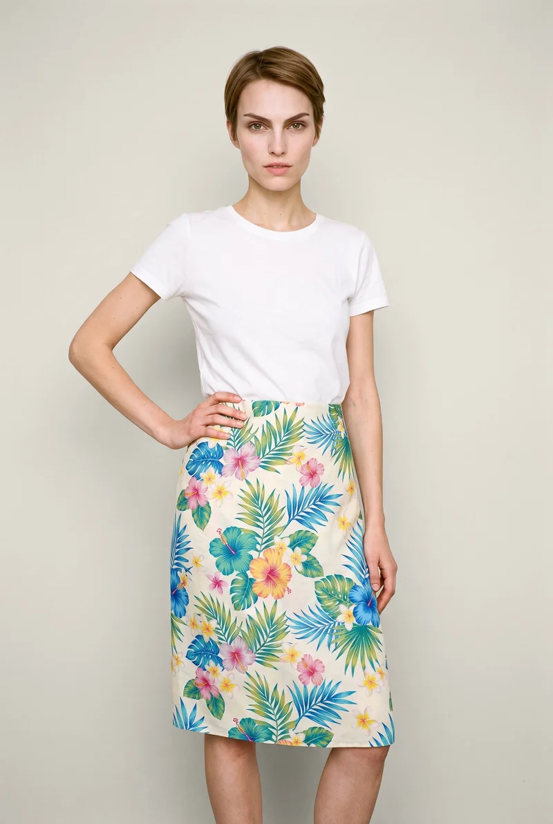 A 26-year-old Caucasian woman is shown from the front in a three-quarter-length view, wearing a floral print sarong with one hand on her hip. She has a confident expression, with an Oyster Pearl studio-wall backdrop.