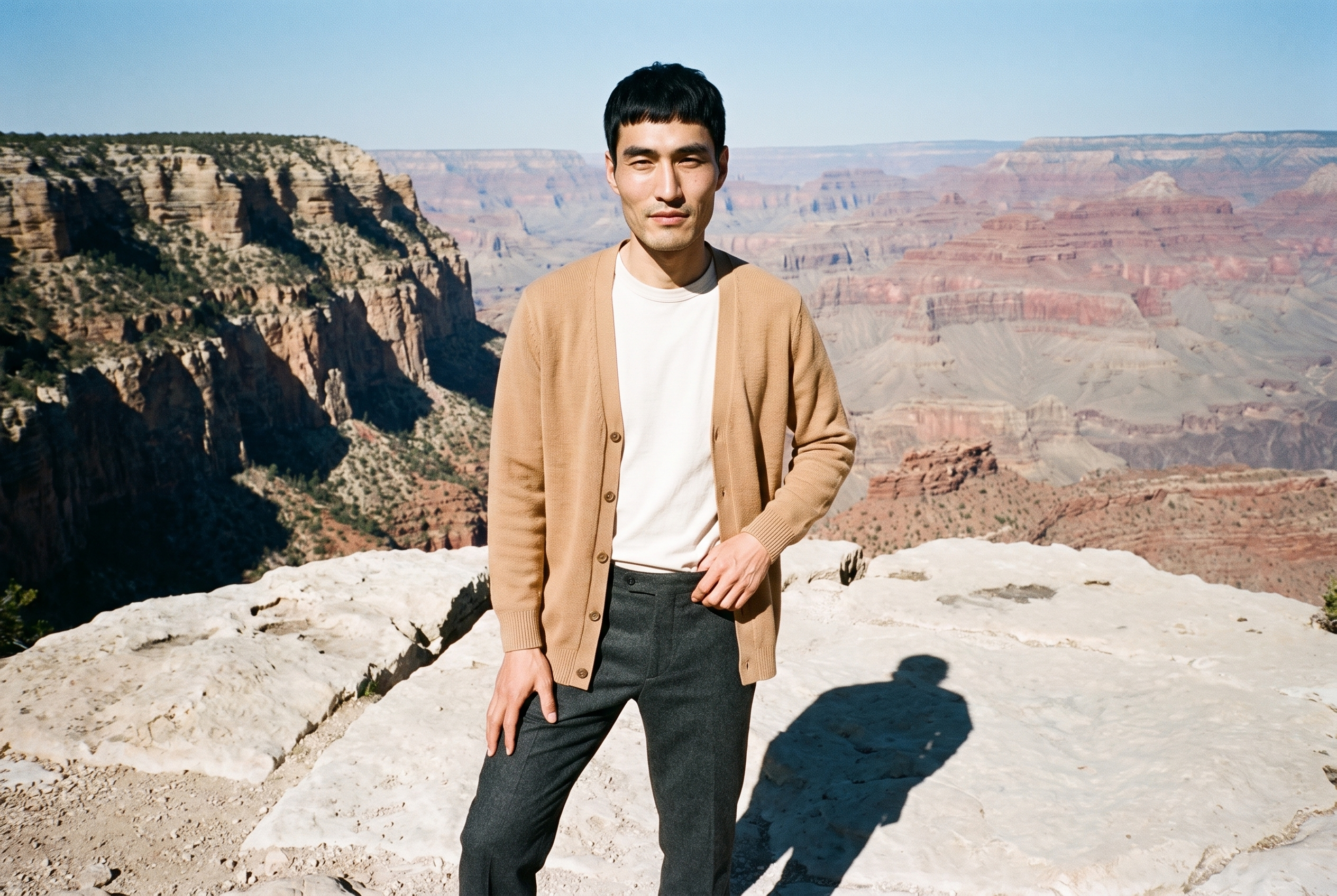 A 37-year-old Chinese man wears a men's camel longline cardigan in a three-quarter-length front view. He poses with one hip angled outward and a confident expression against a Grand Canyon Rim backdrop.