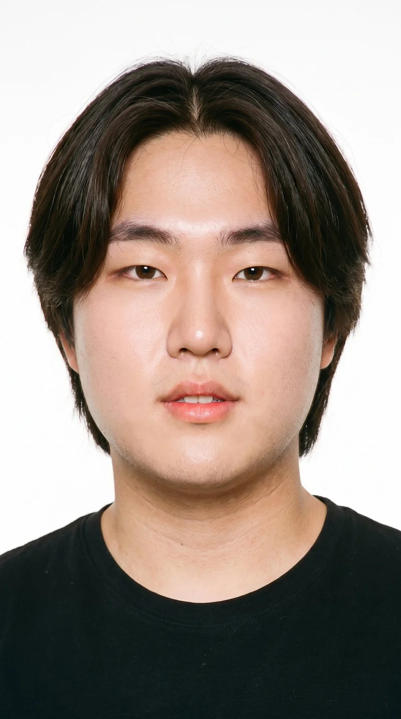 A 20-year-old Korean man with light-tan skin and a neutral undertone has an oval face with balanced proportions and a softly rounded jaw. His medium-thickness eyebrows frame brown eyes, and he has thin lips. His dark-brown hair is divided at the centre and falls evenly to both sides. He is clean-shaven, with smooth skin across the face.