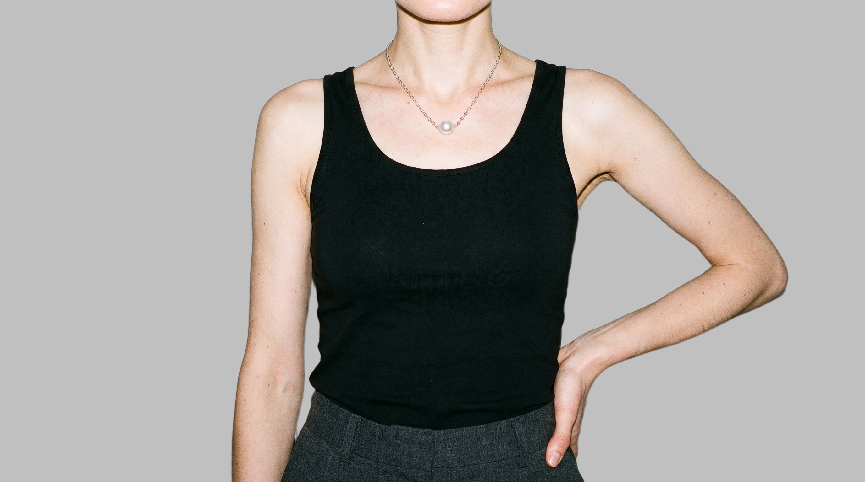 A woman is shown from the torso up in a front view, wearing a pearl pendant with one hand on her hip. The image has a flat Silver Mist backdrop.