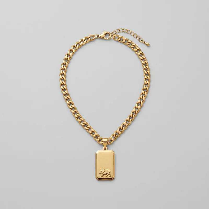 A complete gold pendant necklace is laid out in an oval shape. It features a continuous flat curb-link chain, a front-centered rounded rectangular tag pendant with a raised border and smooth face, and a raised lion emblem near the lower portion. The lobster clasp, adjustable extension chain, and teardrop end charm are also visible.