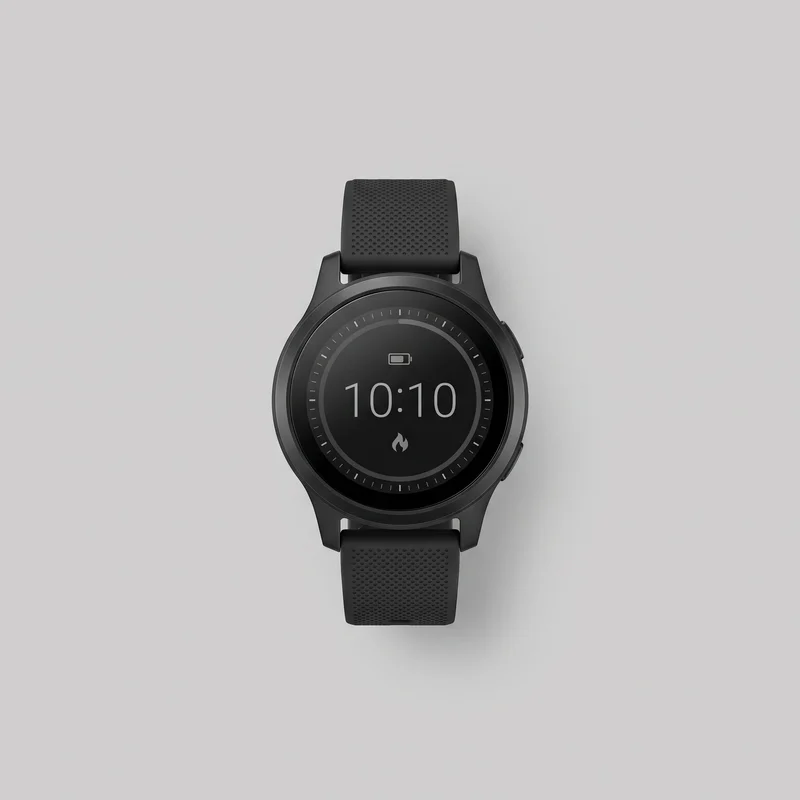 A complete front view of a black round digital smartwatch with its upper and lower strap sections visible. The circular touchscreen has a raised concentric bezel, a large digital time readout, a minute-tick ring, a battery icon, and a flame-like icon. Integrated angular lugs, two side controls, and a dense grid of strap perforations are visible.