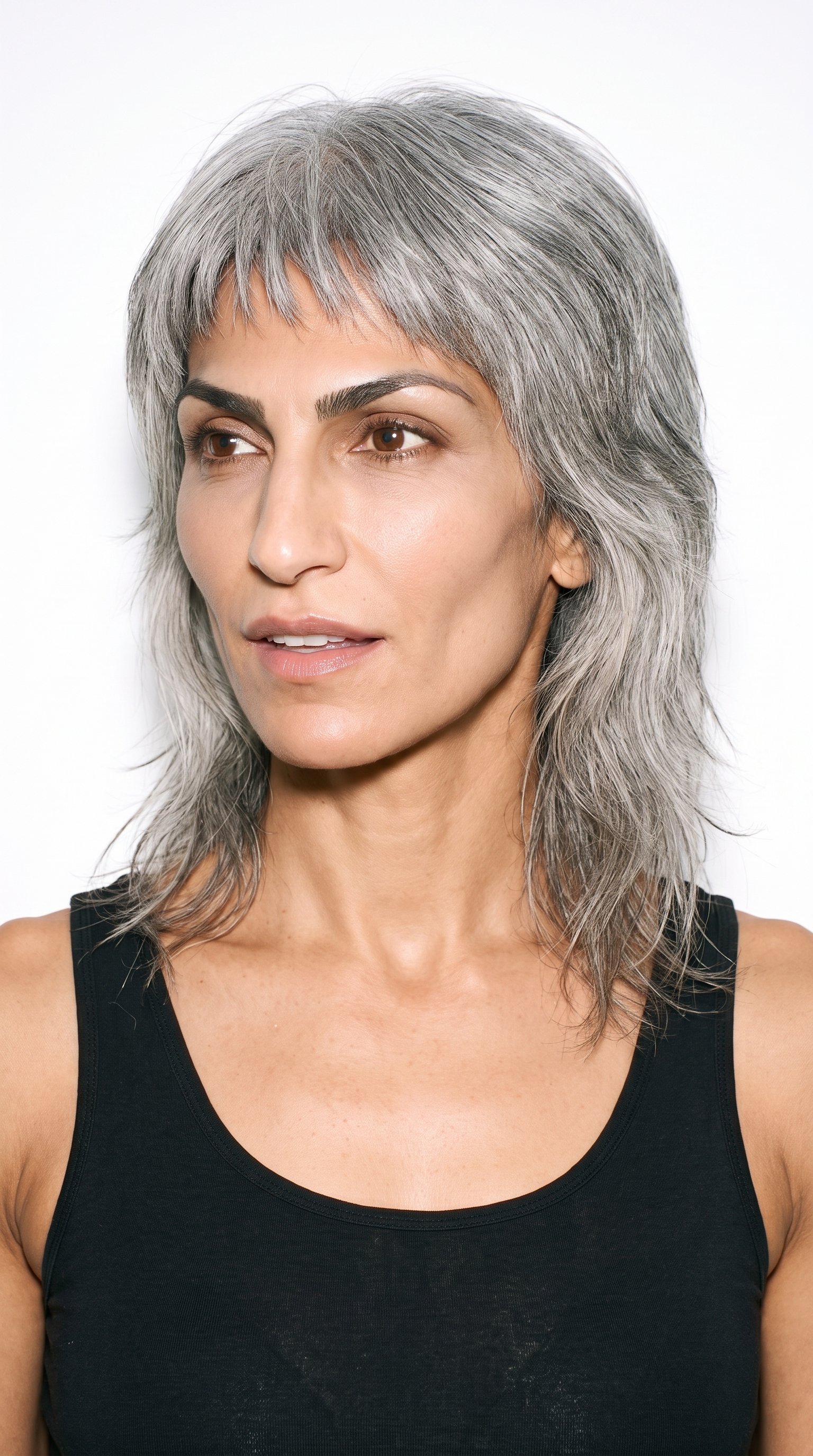 A 42-year-old Arab woman with caramel, medium-brown skin and an olive-green undertone. Her angular face has sharp, defined cheekbones and jawline, with thick eyebrows, brown eyes, and medium lips. She wears gray hair in a layered wolf cut with volume at the crown and tapered, textured lengths.