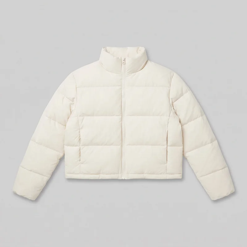 A cream men's cropped puffer jacket is shown laid flat in a complete front view. It has a relaxed boxy silhouette, a high padded stand collar, dropped shoulders, long wide sleeves, a full-length central zipper extending into the collar, horizontal quilted panels across the body and sleeves, vertical side panel seams near the lower front, and a straight cropped hem.